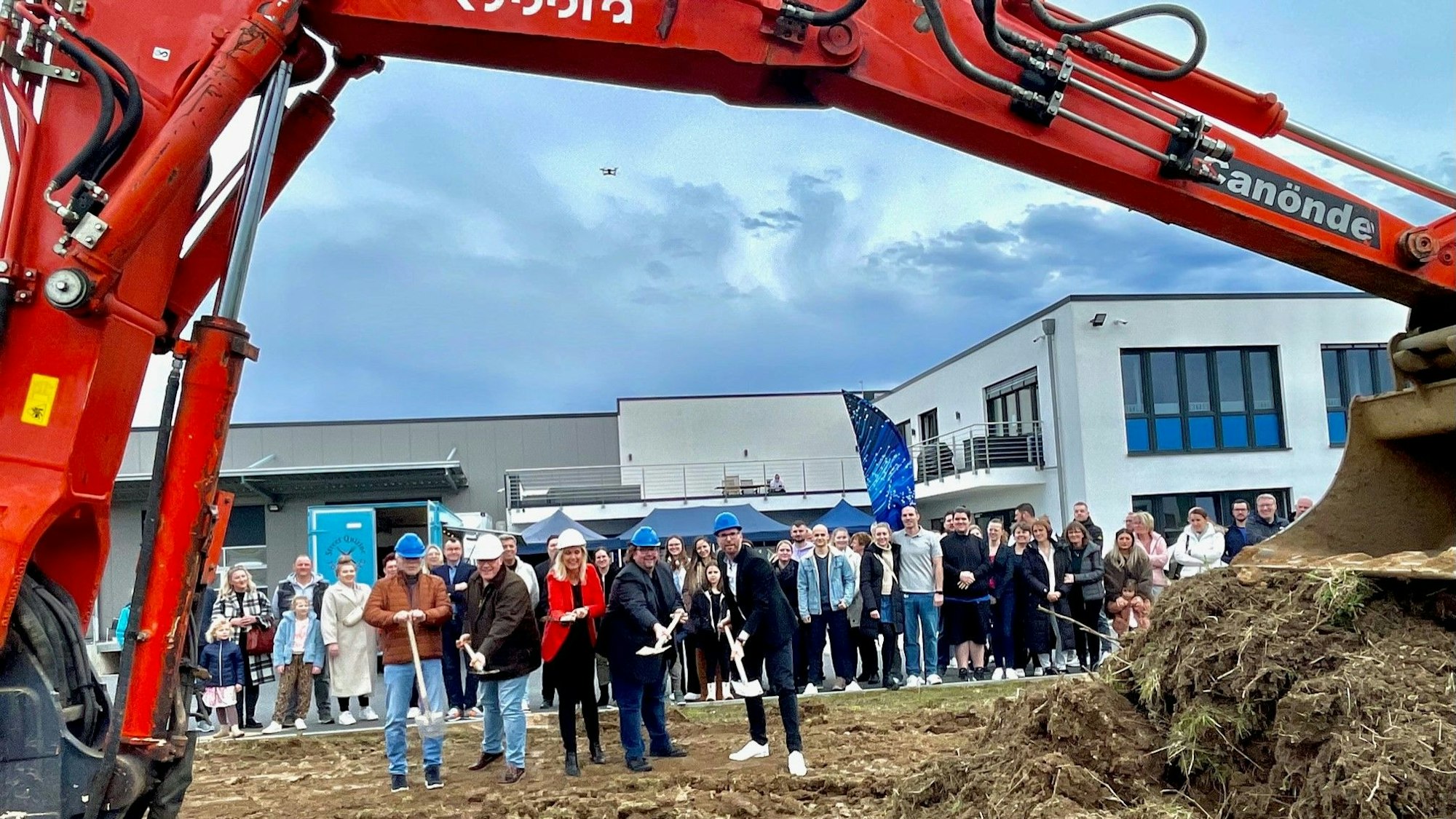 Durch den Arm des Baggers fällt der Blick auf die Akteure des symbolischen Spatenstichs im Wirtschaftspark.
