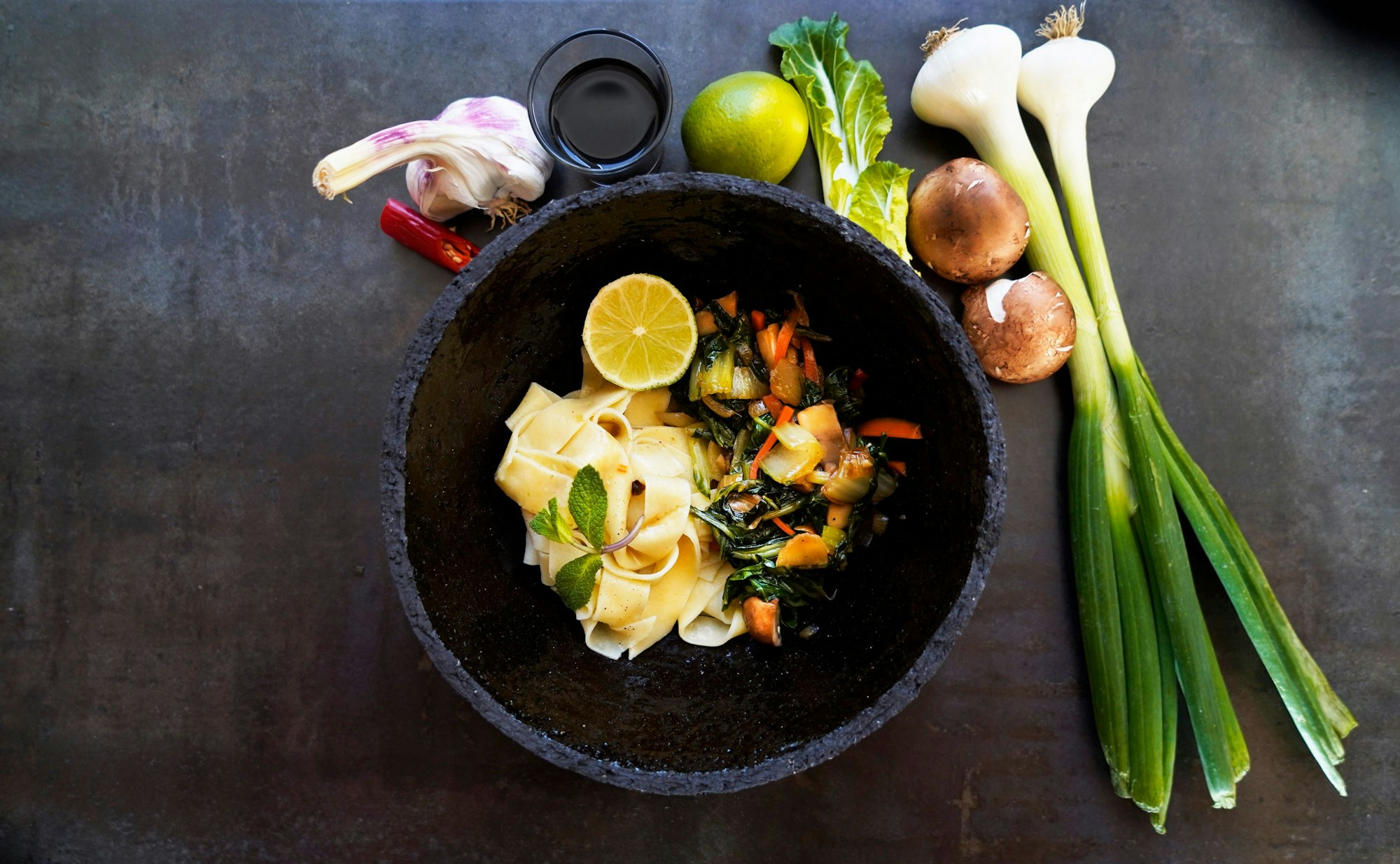 In einer Schüssel liegen die Tagliatelle mit Gemüse. Neben dem Teller liegen die Zutaten als Deko.