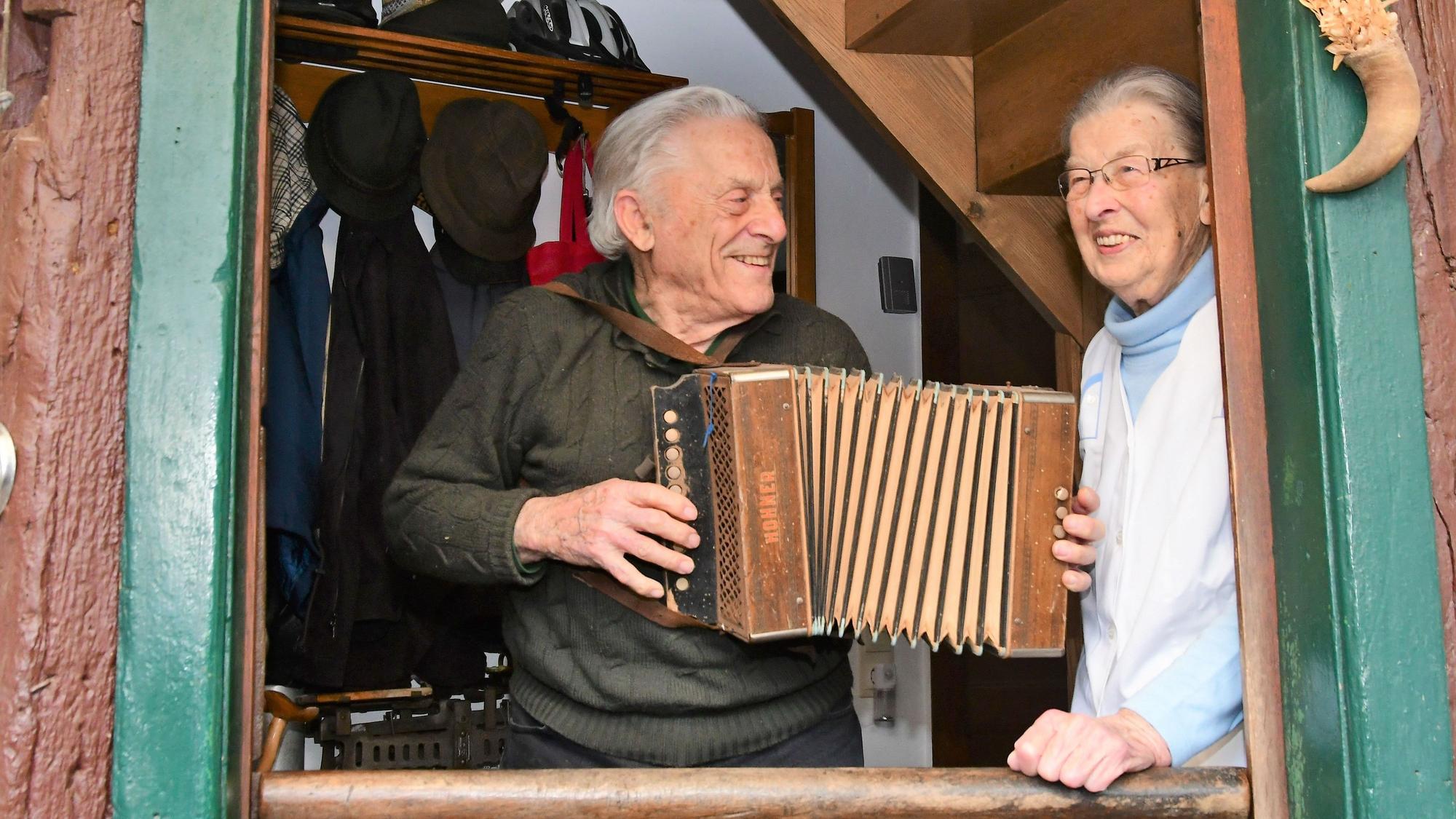 Opa Ferdi und Oma Agnes schauen aus dem Fenster ihres Fachwerkhauses. Opa Ferdi spielt auf dem Akkordeon.