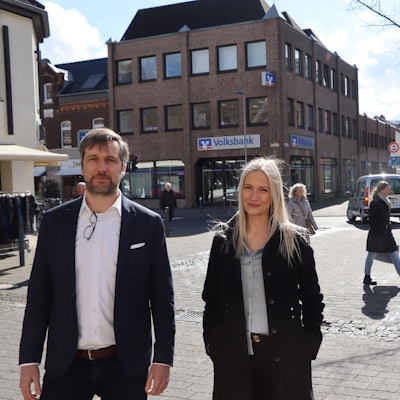 Die Juristen Alina Kriechel und Alrik Haug finden, dass das Linksabbiegeverbot schnell wieder aufgehoben werden soll. Sie stehen in Erftstadt-Lechenich. Im Hintergrund ist zu sehen, dass ein Pkw links abbiegt, obwohl das Verkehrszeichen einen Pfeil nach rechts zeigt.