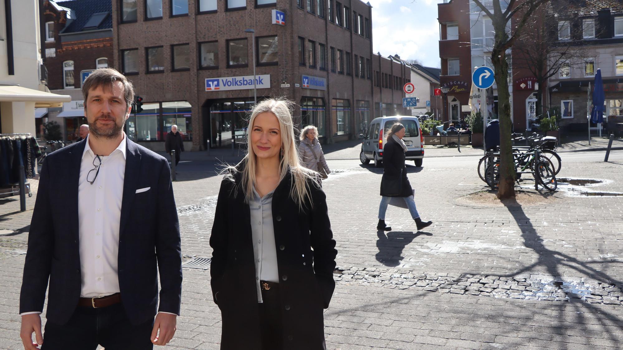 Die Juristen Alina Kriechel und Alrik Haug finden, dass das Linksabbiegeverbot schnell wieder aufgehoben werden soll. Sie stehen in Erftstadt-Lechenich. Im Hintergrund ist zu sehen, dass ein Pkw links abbiegt, obwohl das Verkehrszeichen einen Pfeil nach rechts zeigt.