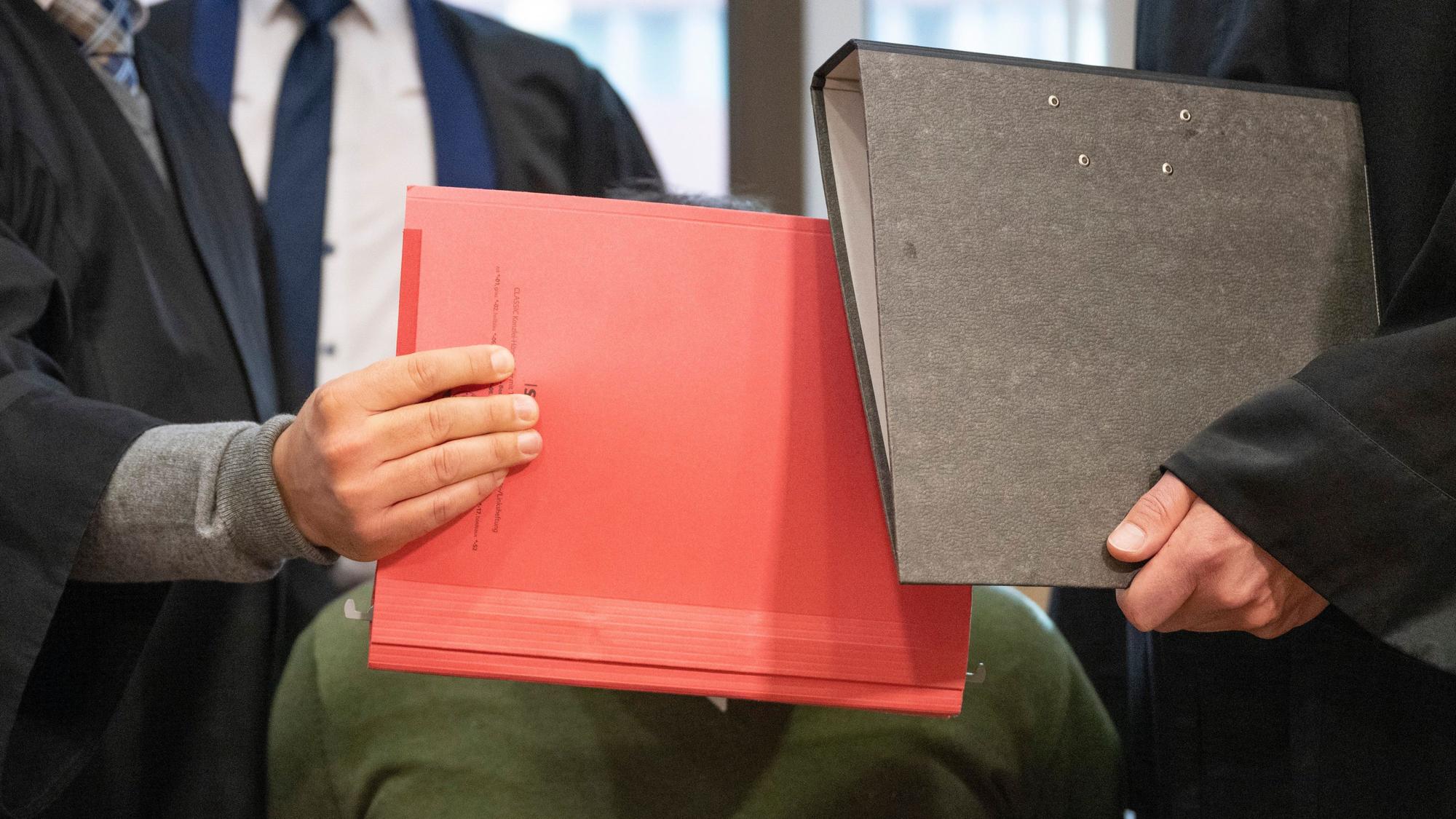 Aktenmappen verstecken das Gesicht des Angeklagten im Verhandlungssaal