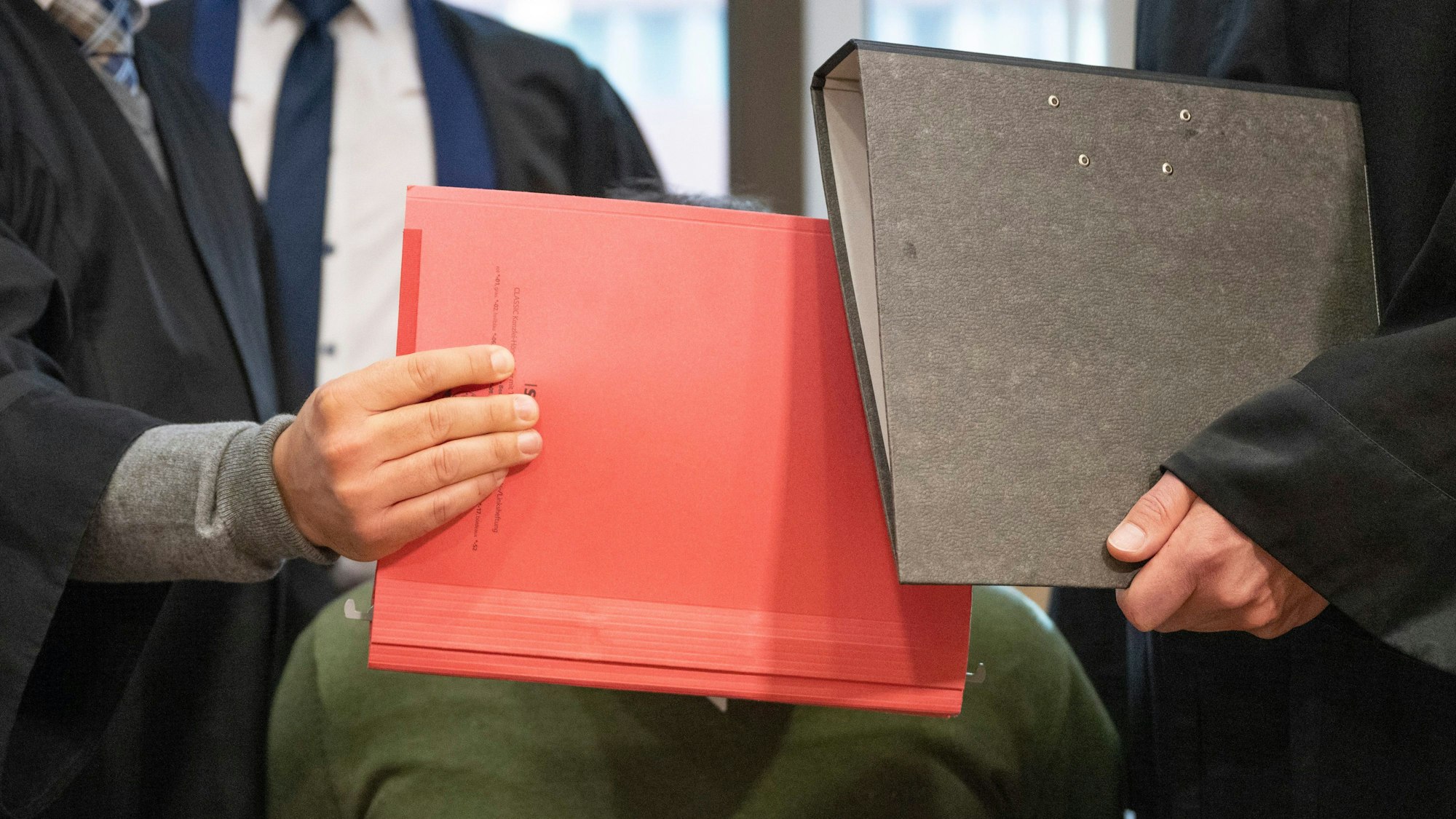 Aktenmappen verstecken das Gesicht des Angeklagten im Verhandlungssaal