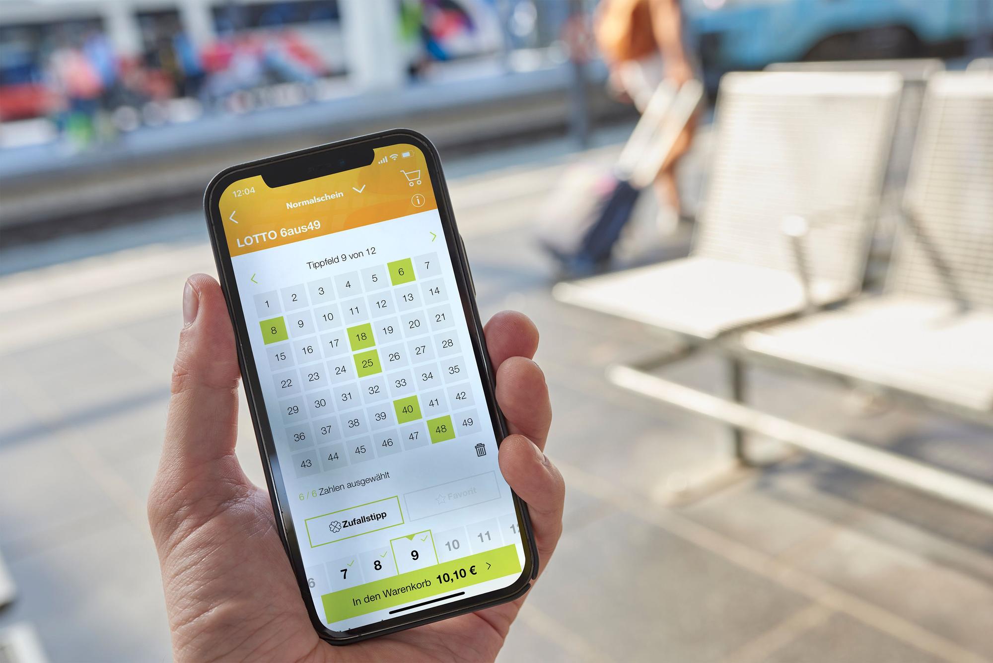 Mann hält Smartphone mit Lotto 6aus49 auf dem Display.