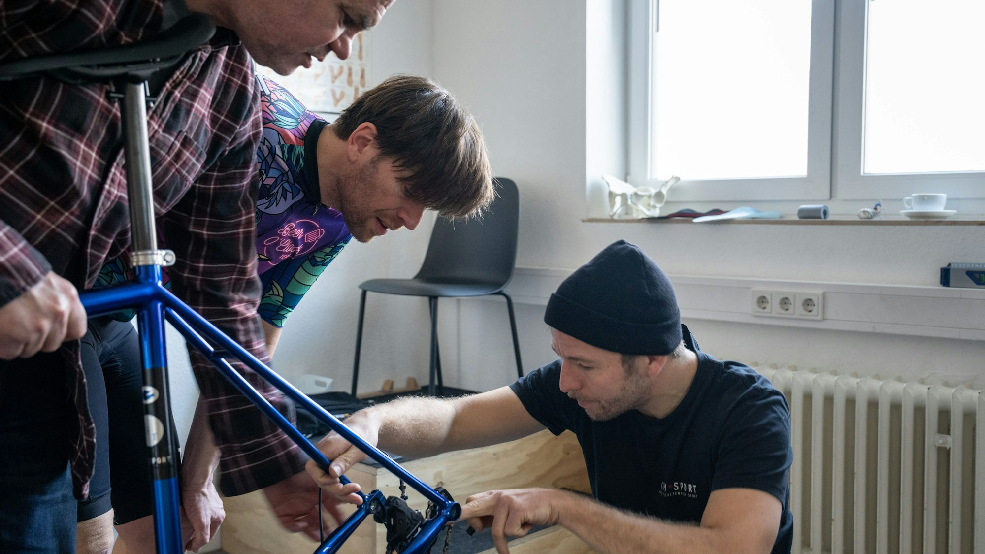 James Buckley, Tim Farin und Sebastian Klaus beugen sich über den Rahmen eines Fahrrads.
