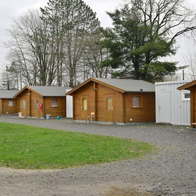 Vier hölzerne Blockhütten, davor ein Picknicktisch und eine Kinderschaukel.