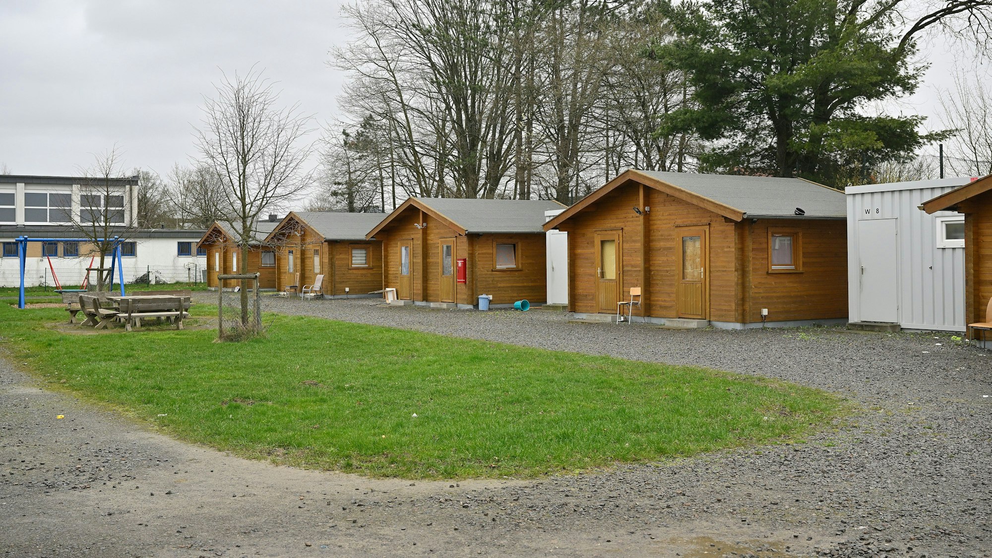 Vier hölzerne Blockhütten, davor ein Picknicktisch und eine Kinderschaukel.