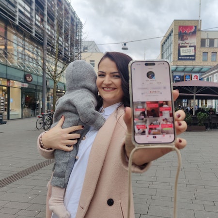 Die Bergisch Gladbacherin Mumfluencerin hält ihr Smartphone in die Kamera, ihr Kind träge sie auf dem anderen Arm.