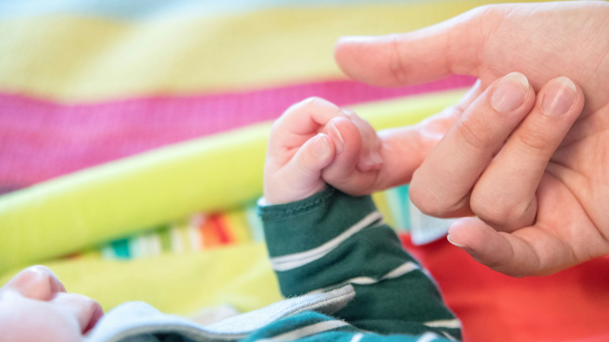 Ein Baby nimmt die Hand eines Erwachsenen.