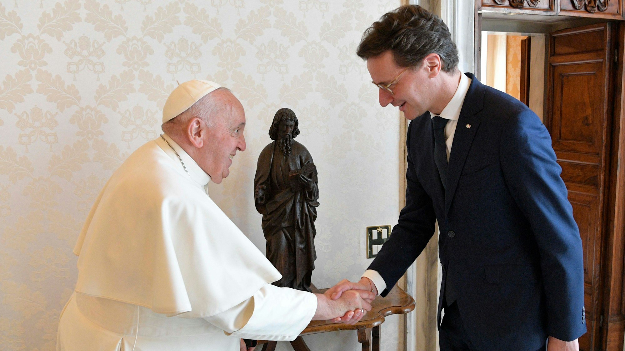 Hendrik Wüst und Papst Franziskus schüttel sich lächelnd die Hände.