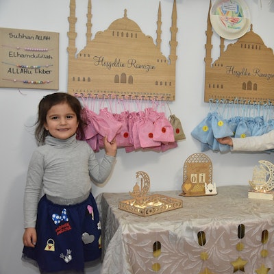 Zwei kleine Mädchen stehen vor Ramadan-Dekorationen. In dreißig Säckcken, die unter einem hölzernen Moschee-Schild aufgehangen sind, erwarten sie Geschenke.
