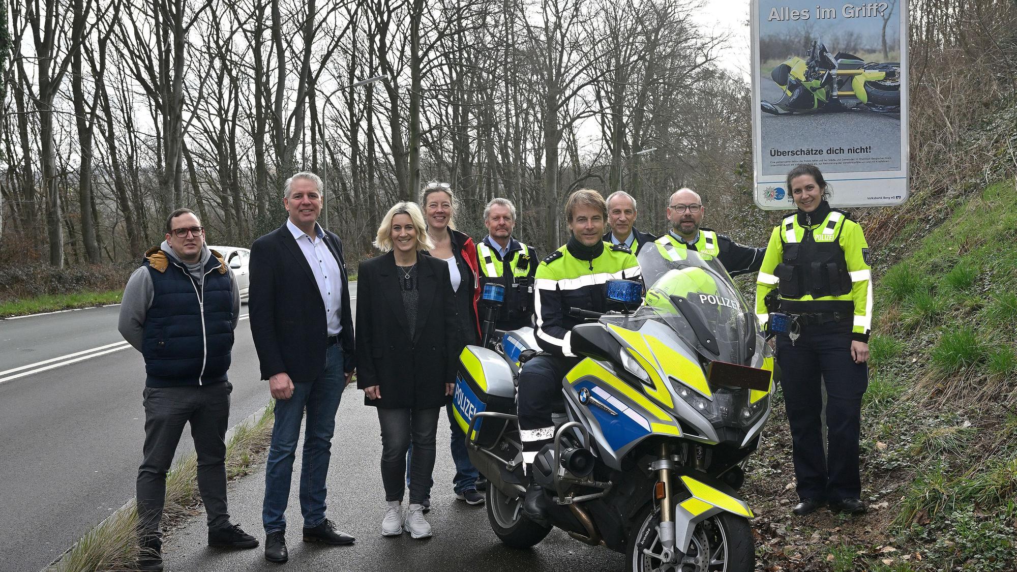 Polizeibeamtinnen und -beamte sowie Vertreter von Gemeinden, Städten und Kreis stehen vor einem neuen Schild, das Motorradfahrer zu Vorsicht anhalten soll. Über dem Bild eines verunglückten Motorrads ist der Schriftzug„ Alles im Griff?“ zu lesen.