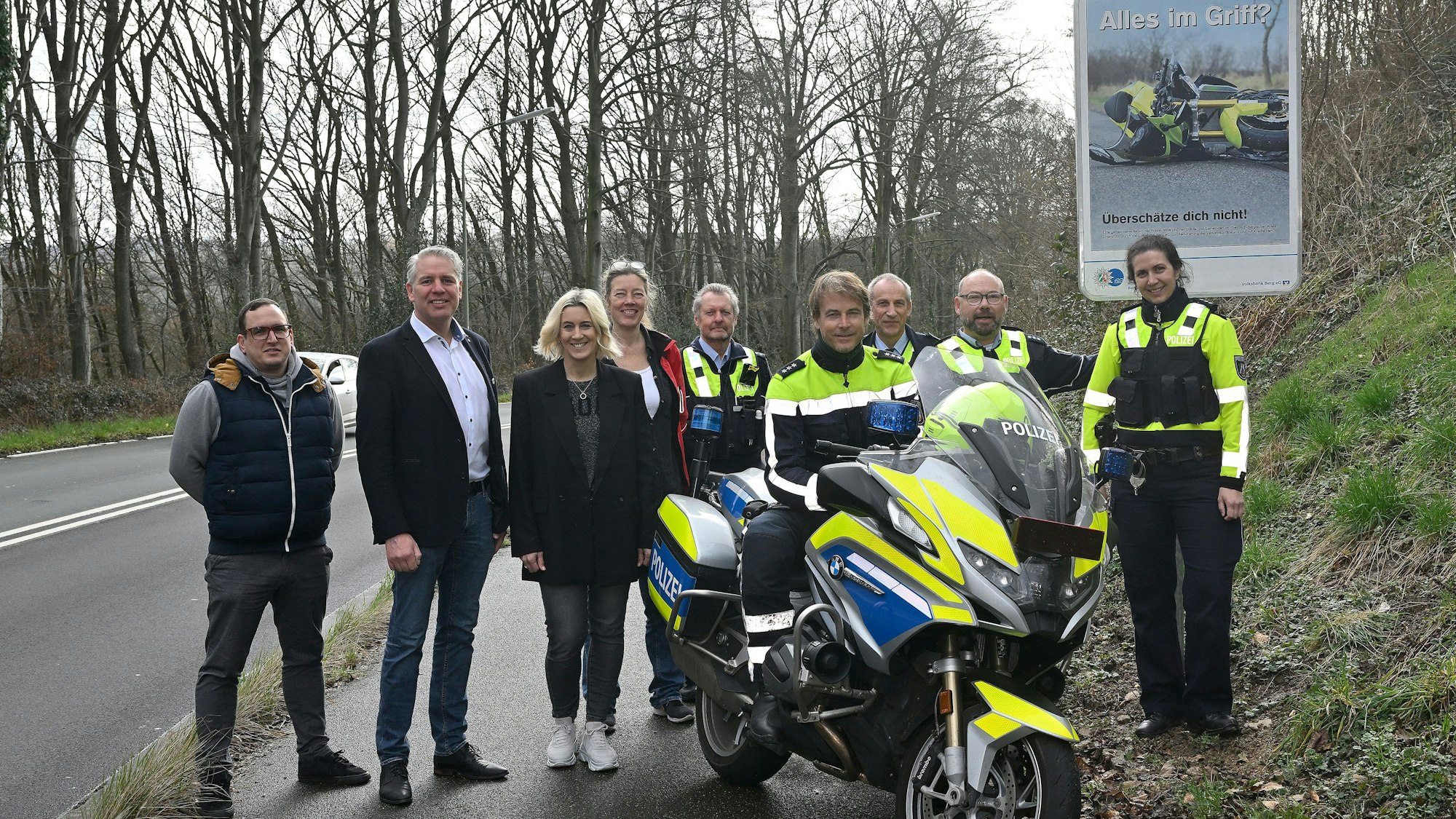 Polizeibeamtinnen und -beamte sowie Vertreter von Gemeinden, Städten und Kreis stehen vor einem neuen Schild, das Motorradfahrer zu Vorsicht anhalten soll. Über dem Bild eines verunglückten Motorrads ist der Schriftzug„ Alles im Griff?“ zu lesen.