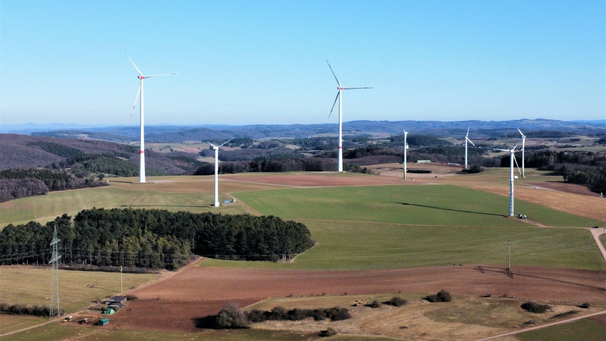 Windräder drehen sich in einer ländlichen Gegend unter blauem Himmel.