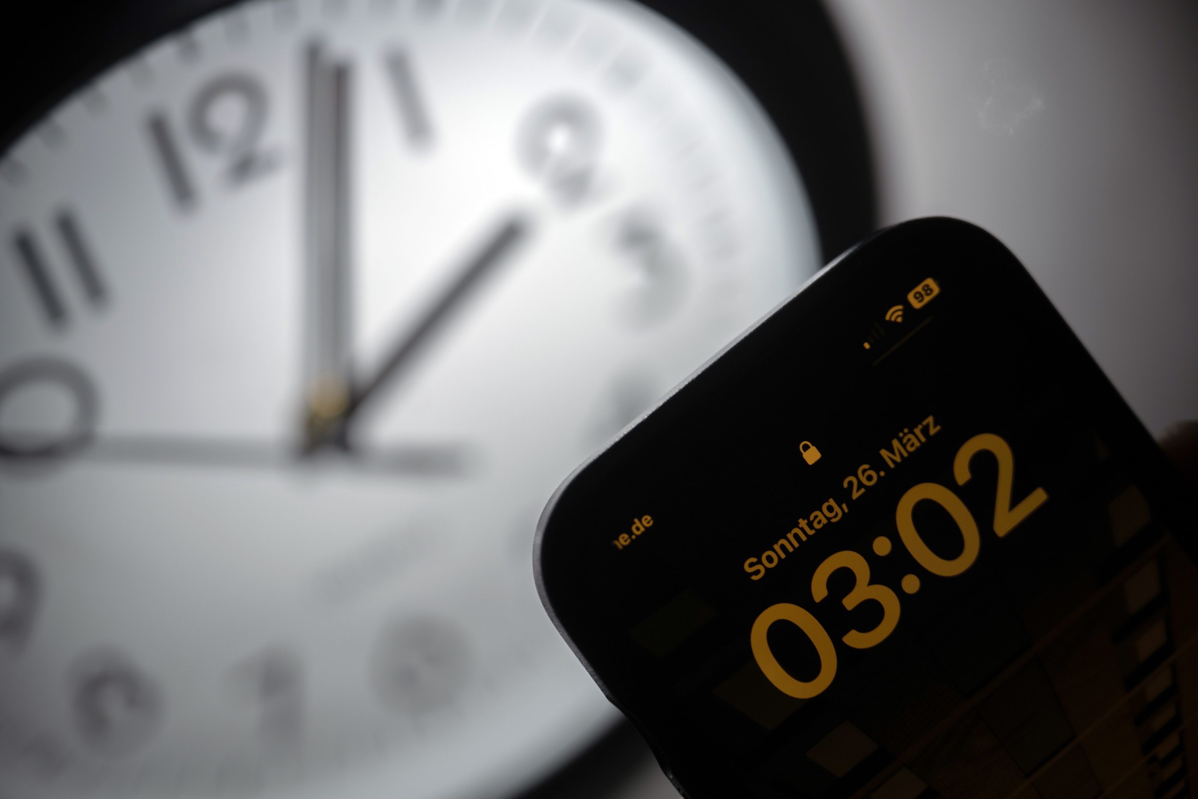 Ein Smartphone zeigt die Uhrzeit «03:03» an, während auf einer analogen Uhr noch 02:03 Uhr ist.