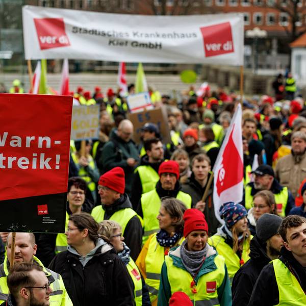 Man sieht Menschen in Warnkleidung und mit Schildern.