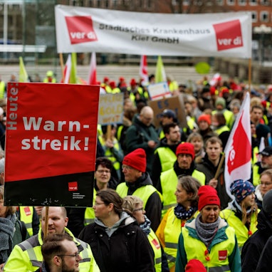 Man sieht Menschen in Warnkleidung und mit Schildern.