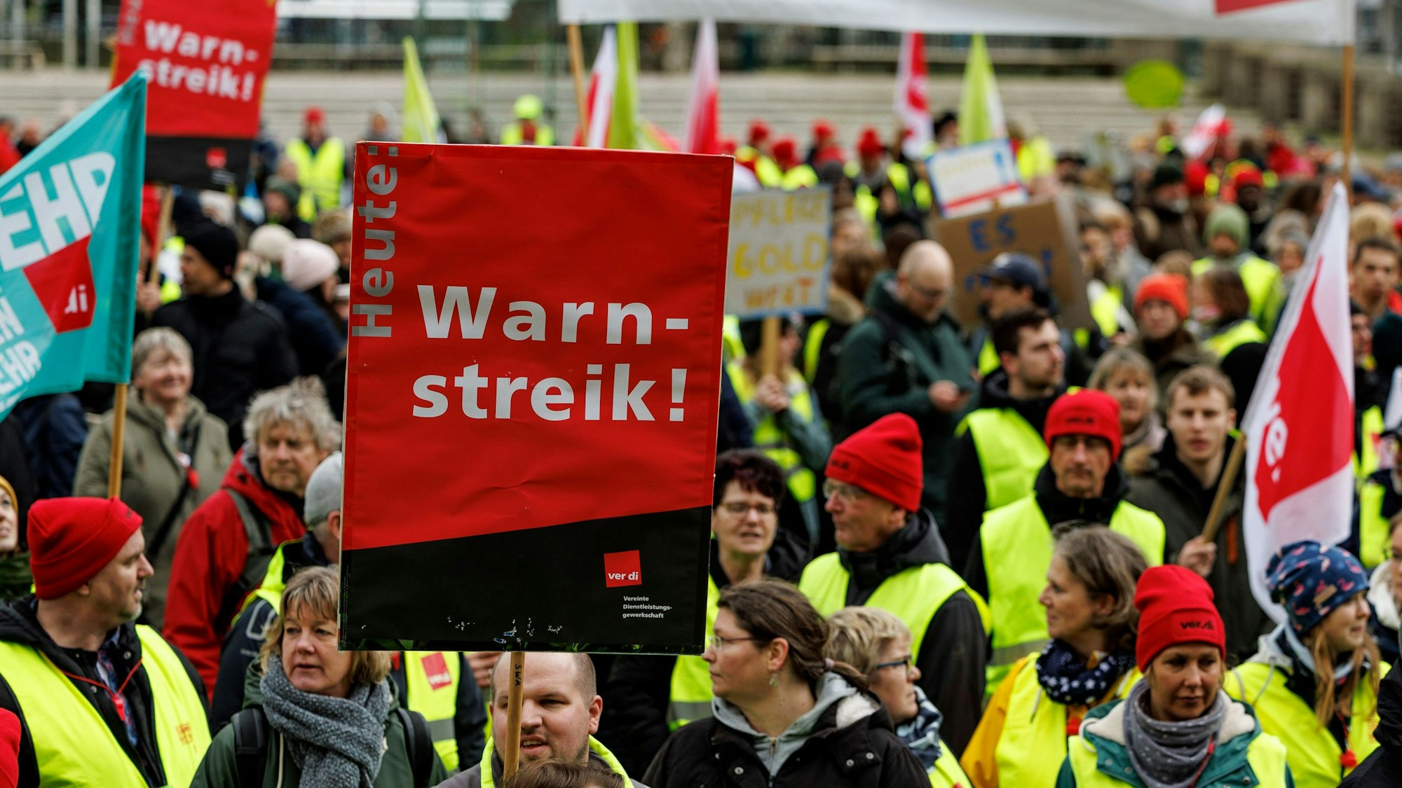 Man sieht Menschen in Warnkleidung und mit Schildern.