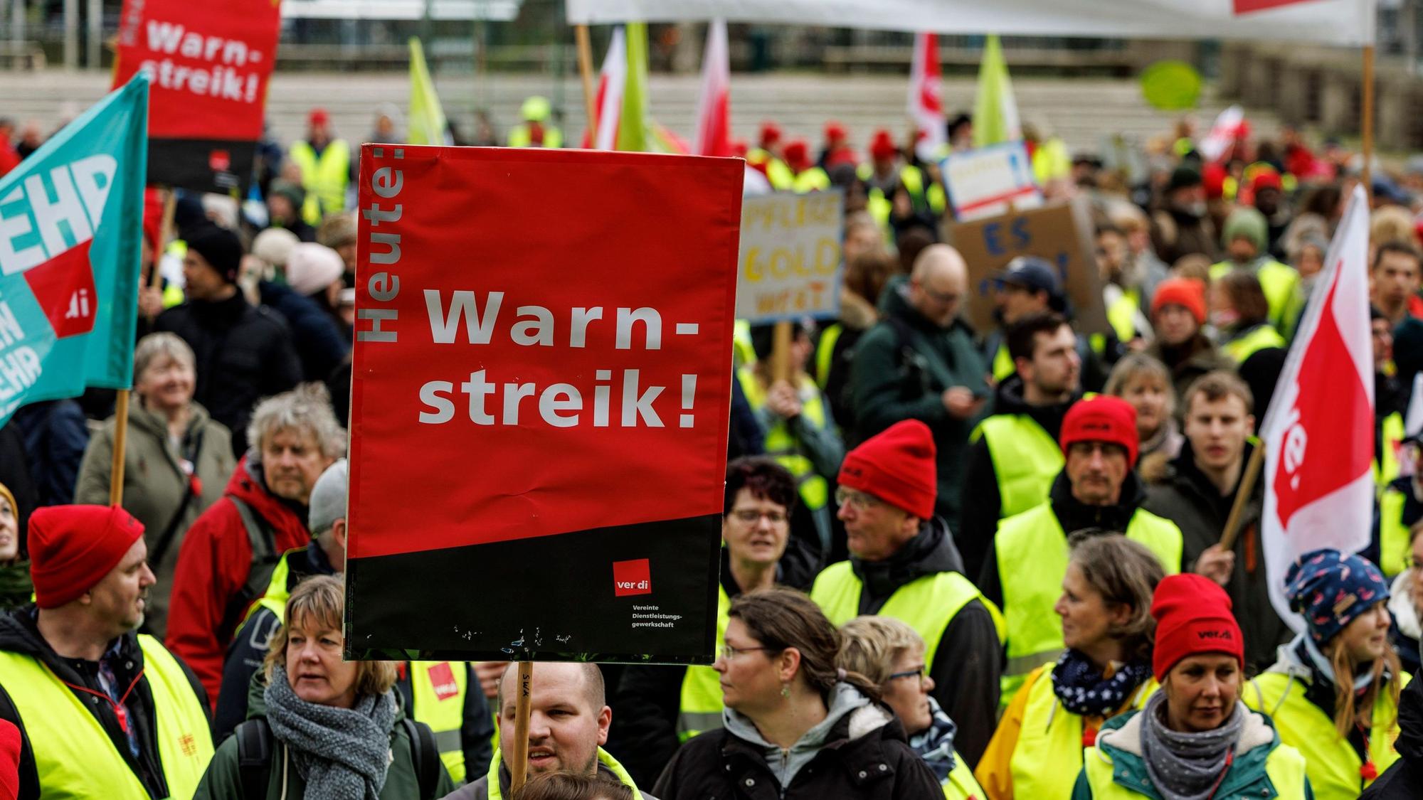 Man sieht Menschen in Warnkleidung und mit Schildern.