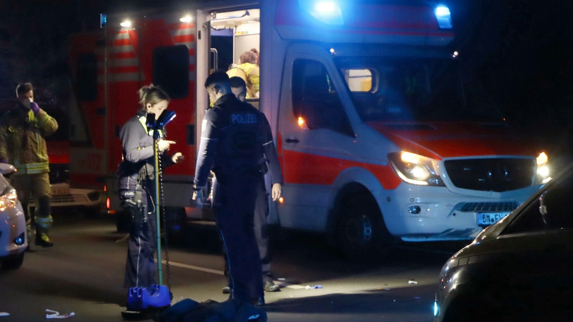 Polizisten stehen an einer Unfallstelle und sichern Spuren. Im Hintergrund steht ein Rettungswagen.