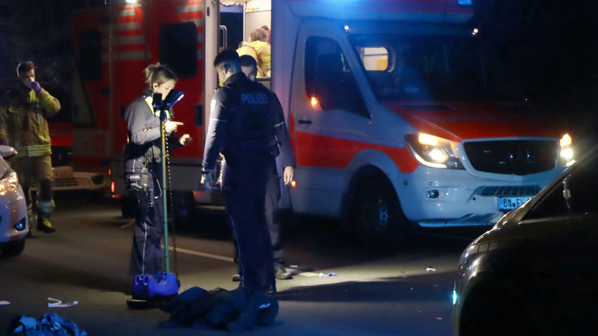Es ist ein Rettungswagen zu sehen. Davor stehen mehrere Polizisten und Sanitäter an der Unfallstelle.