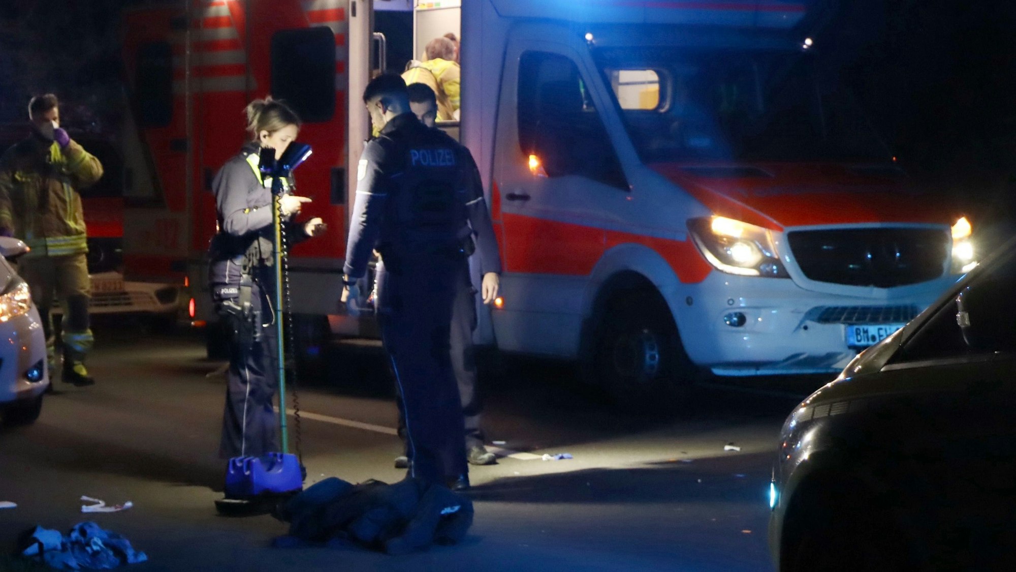 Im Dunkeln steht ein beleuchteter Rettungswagen auf der Straße, davor stehen drei Einsatzkräfte.