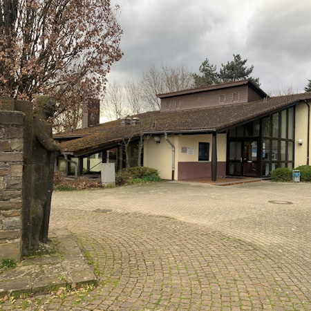 An einem gepflasterten Platz steht ein Gebäude mit einem heruntergezogenen Dach.