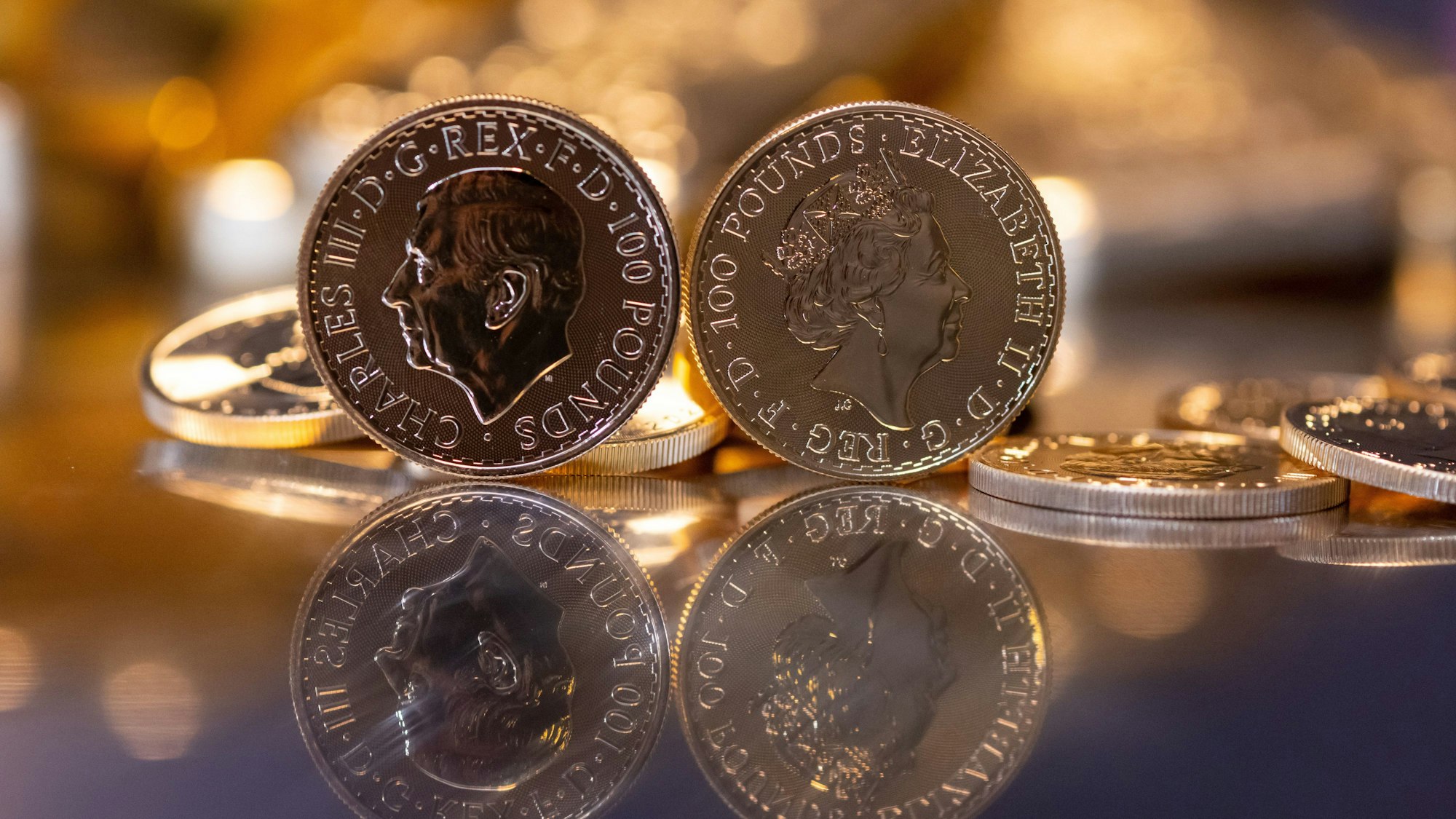 16.03.2023, Bayern, München: Goldbarren und Goldmünzen in unterschiedlicher Größe liegen beim Edelmetallhändler Pro Aurum in einem Tresor auf einem Tisch. Im Vordergrund ist die Goldmünze "Britannia" zu sehen (links mit dem Motiv König Charles III., rechts mit dem Motiv Königin Elizabeth II.)