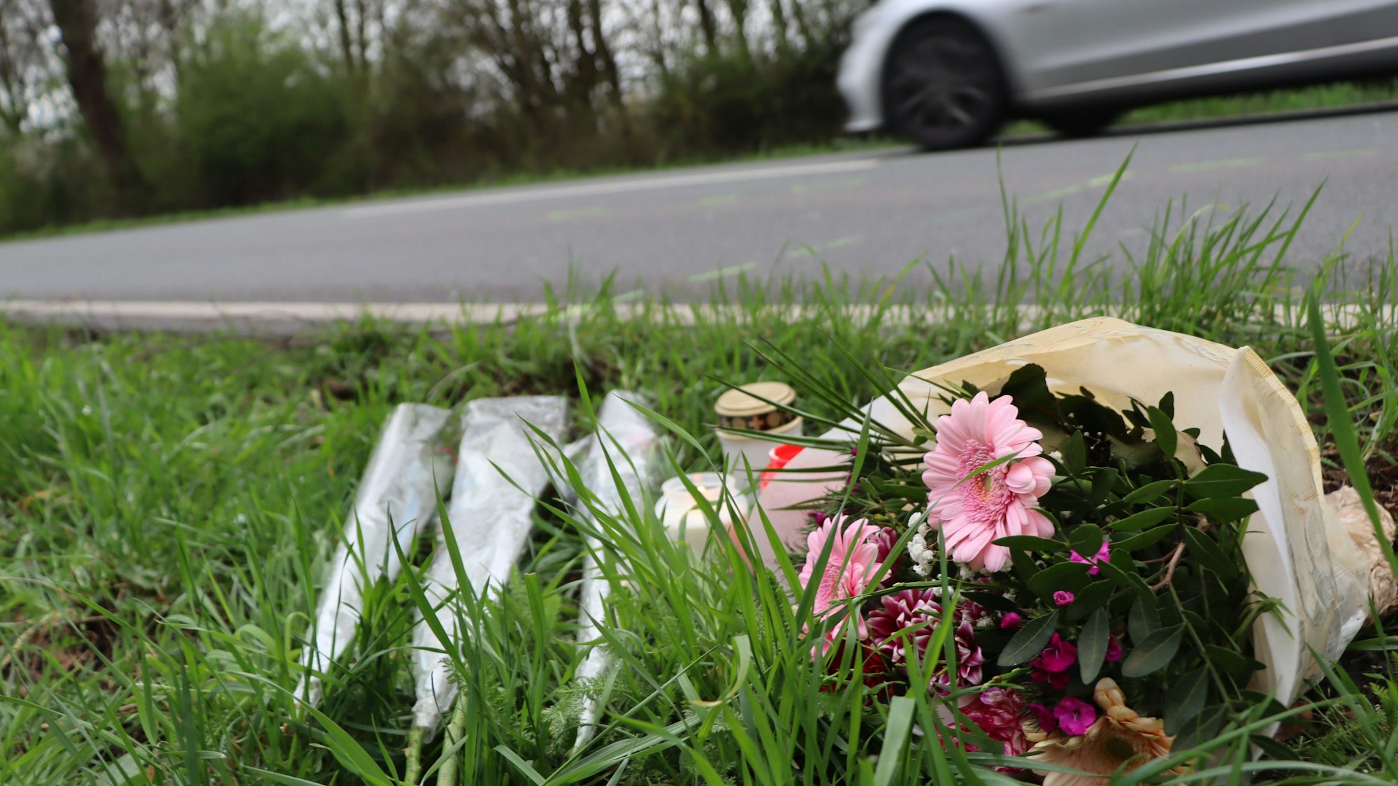 Das Bild zeigt einen Blumenstrauß am Straßenrand der Rodenkirchener Straße in Wesseling. Dort wurde im März ein 20-Jähriger überfahren.