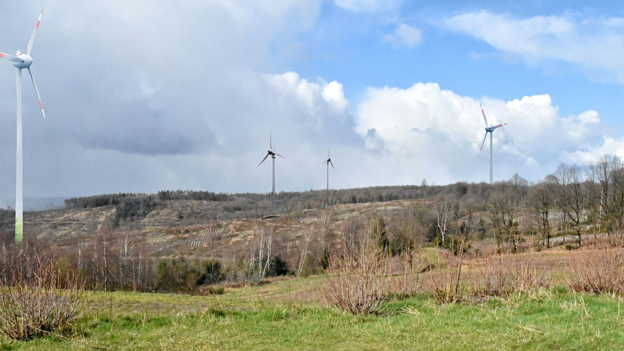Vier Windkraftanlangen stehen auf einer Höhe. Es handelt sich um eine Fotomontage.