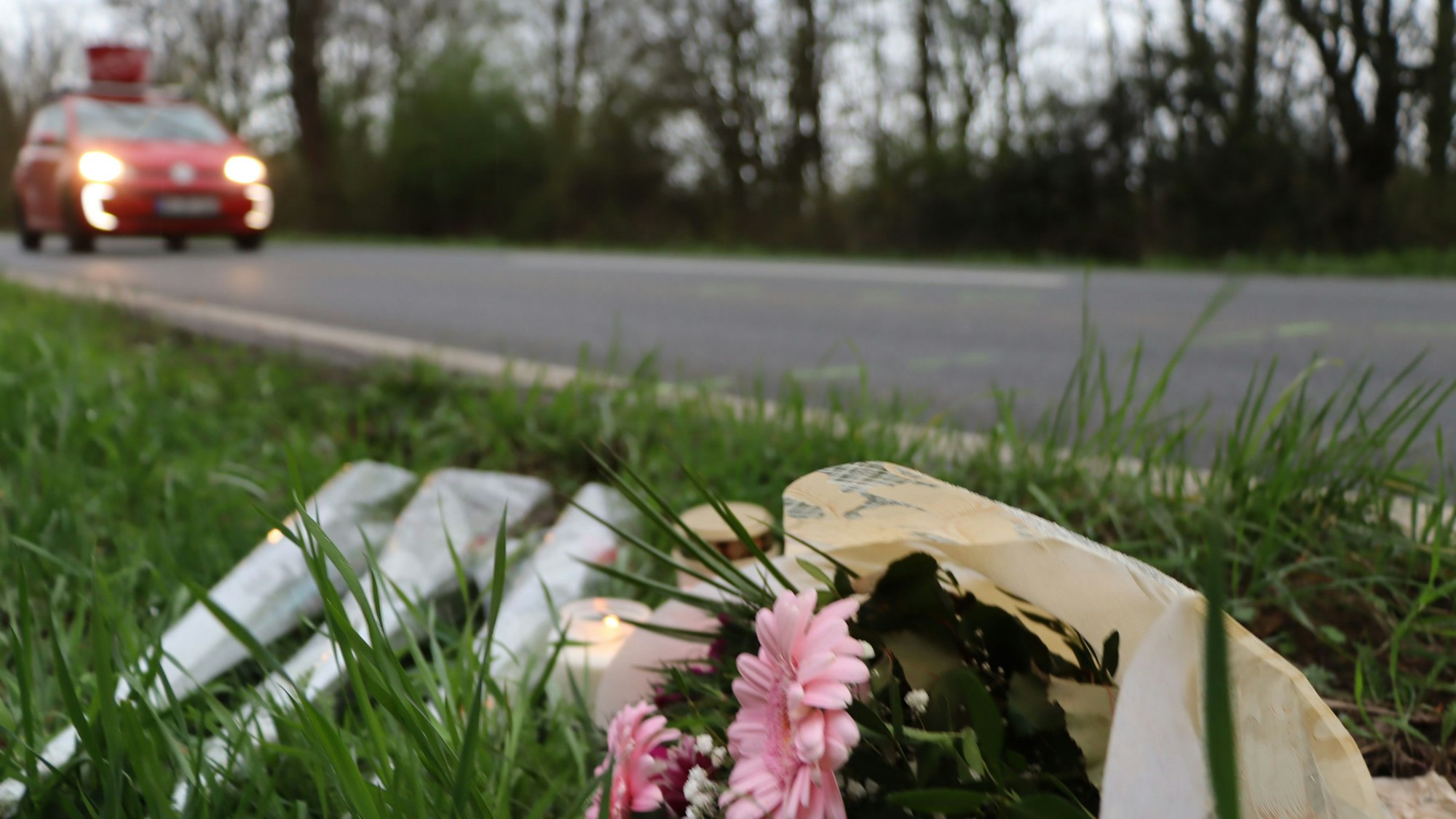Mehrere Blumensträuße liegen neben einer Straße im Gras.