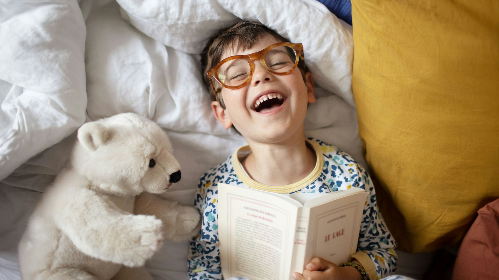 Portrait of a smiling little boy at home, he's wearing adult's glasses and pretending to read his parent's book