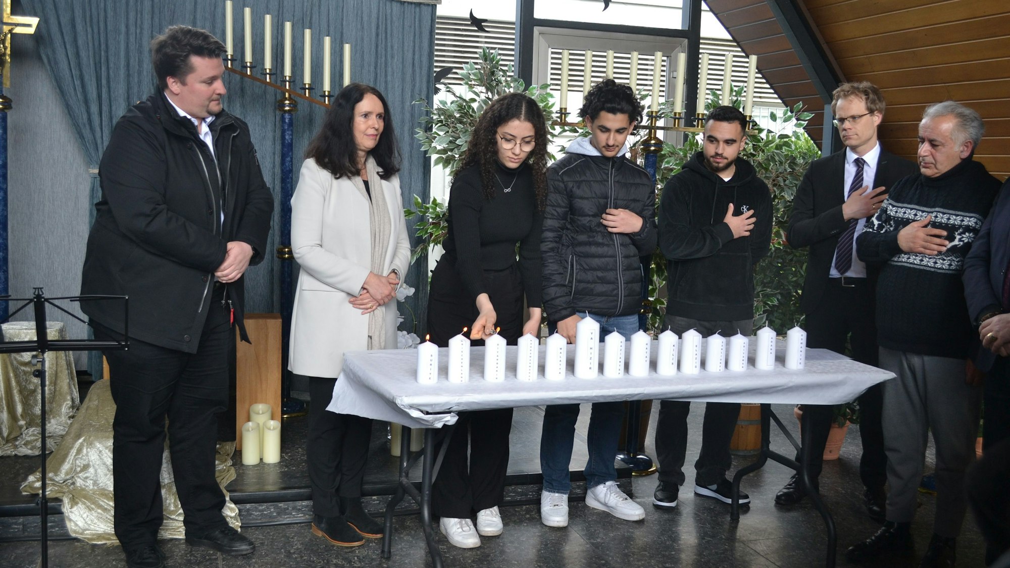 Mehrere Menschen stehen vor einem Tisch mit Kerzen.