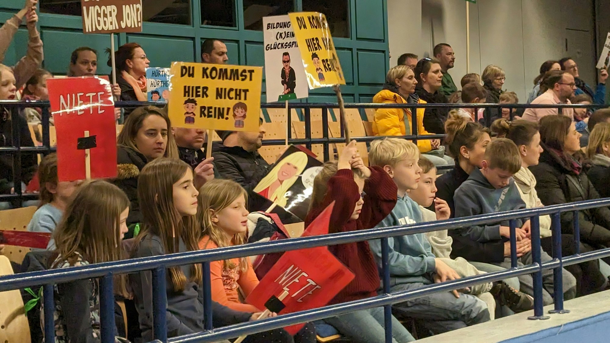 Kinder und Eltern zeigen Protestplakate auf den Zuschauerrängen.