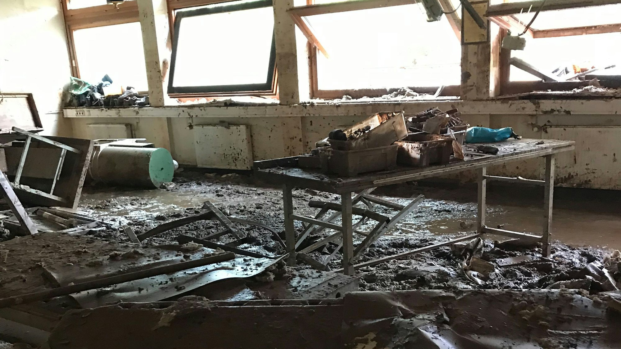 Ein Klassenzimmer des Thomas-Eßer-Berufskolleg in Euskirchen, das von der Flut schwer beschädigt wurde. Der Boden ist mit Matsch bedeckt und die Fenster sind kaputt.