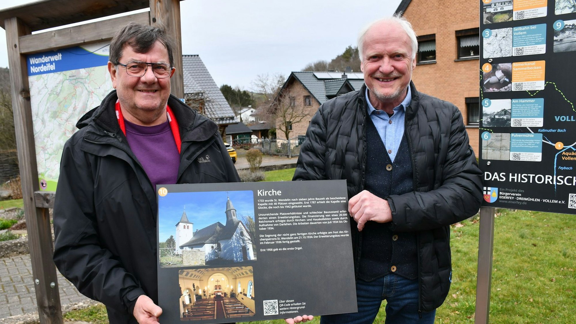 Franz Harperscheid (l.) und Walfried Heinen mit der Infotafel zur Pfarrkirche St. Wendelinus, einer von 18 Sehenswürdigkeiten und historischen Orten in Eiserfey und Umgebung.