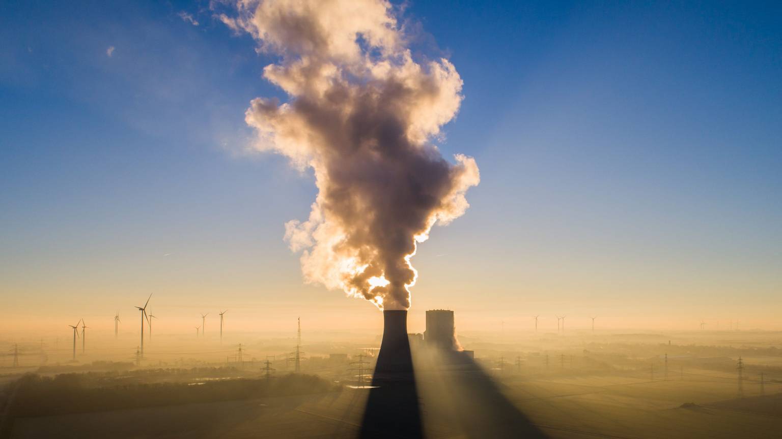 Die Sonne geht hinter dem Kraftwerk Mehrum im Landkreis Peine auf. Im Hintergrund stehen mehrere Windkrafträder.