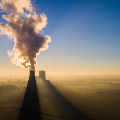 Die Sonne geht hinter dem Kraftwerk Mehrum im Landkreis Peine auf. Im Hintergrund stehen mehrere Windkrafträder.