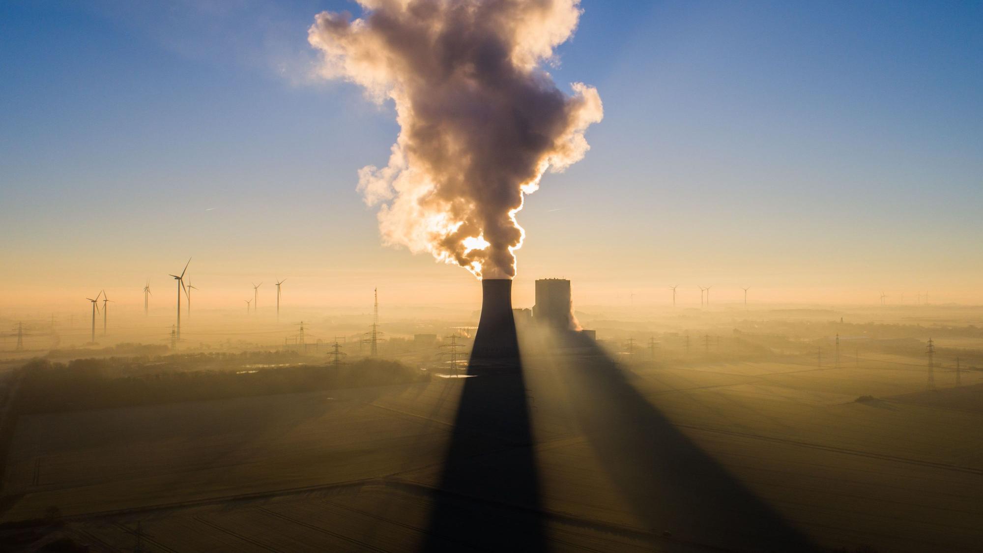Die Sonne geht hinter dem Kraftwerk Mehrum im Landkreis Peine auf. Im Hintergrund stehen mehrere Windkrafträder.