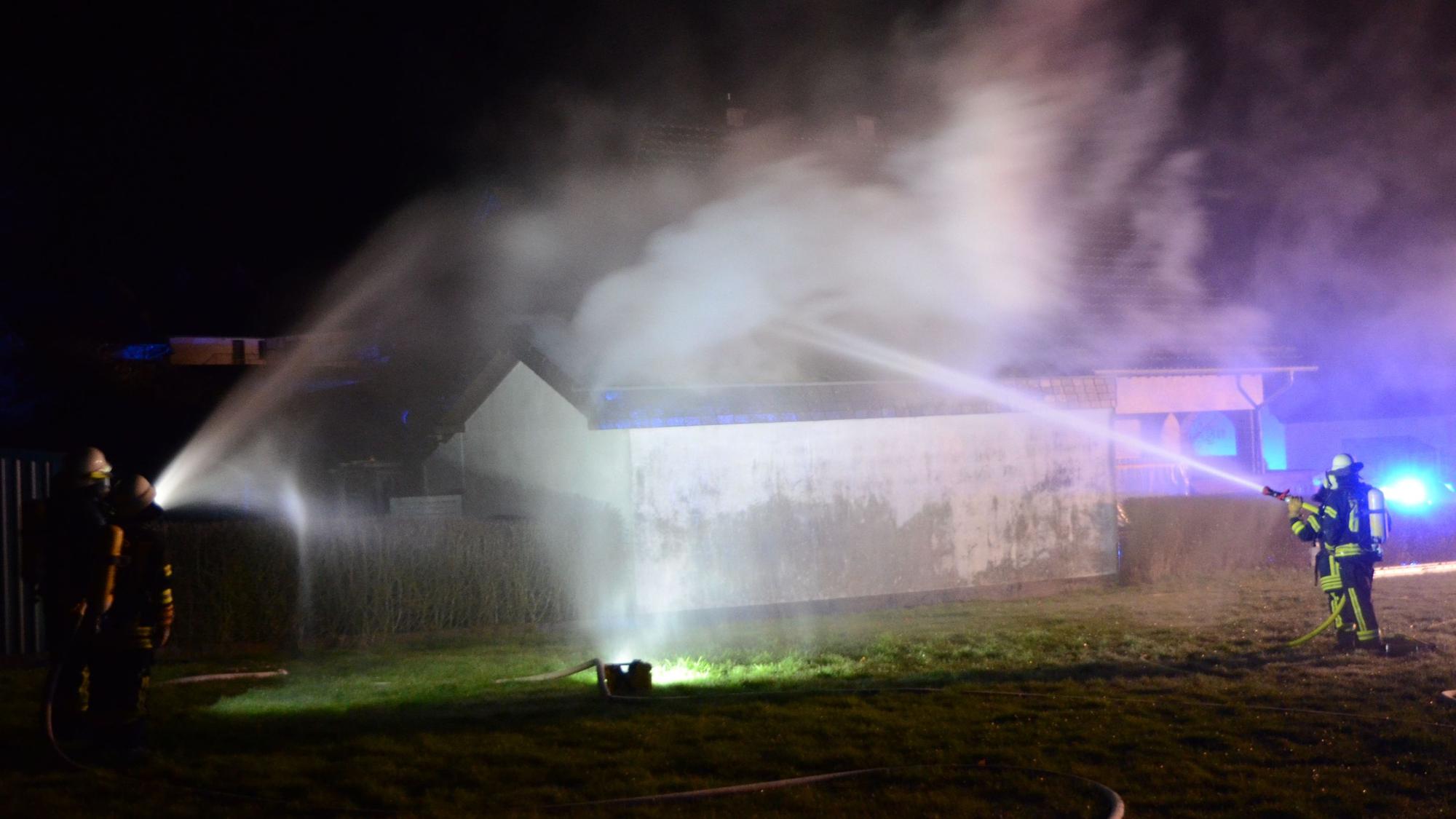 Feuerwehrleute löschen mit Strahlrohren die brennende Garage an einem Wohnhaus in Herhahn.