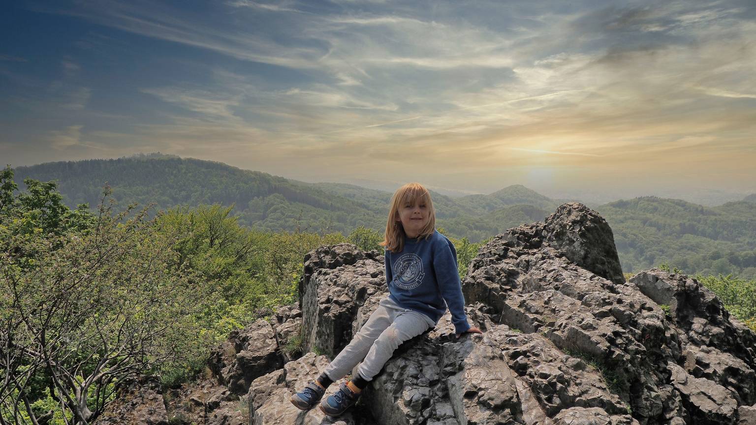 Ein Junge sitzt auf einem Felsen, im Hintergrund ist das Panorama des Siebengebirges zu sehen.