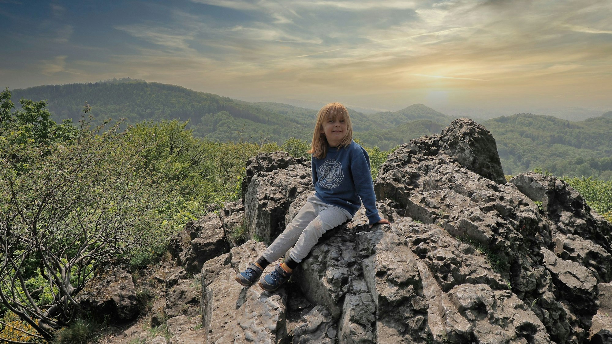 Ein Junge sitzt auf einem Felsen, im Hintergrund ist das Panorama des Siebengebirges zu sehen.