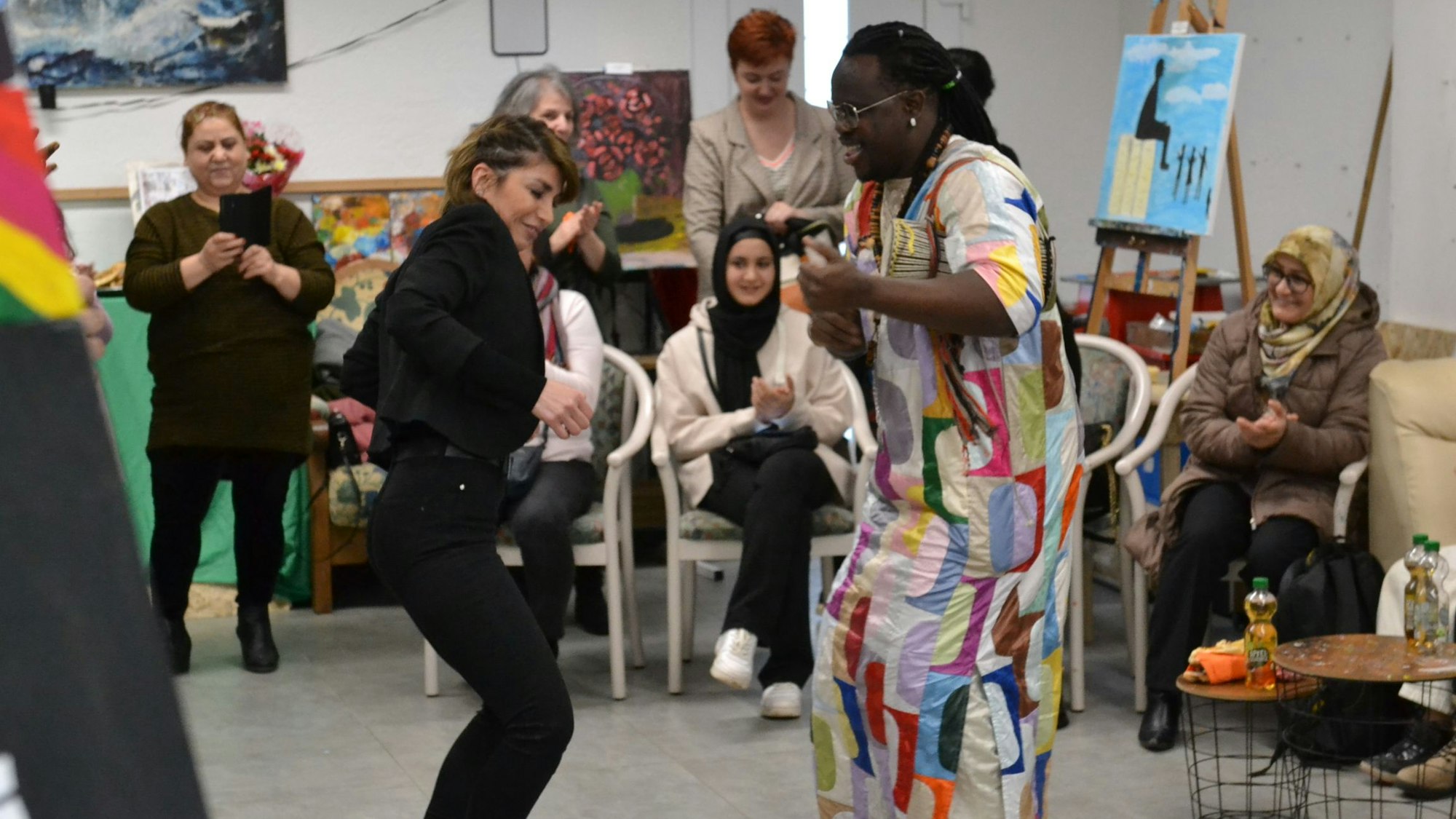 Zwei Menschen tanzen in einem Raum, im Hintergrund Menschen und Kunstwerke.