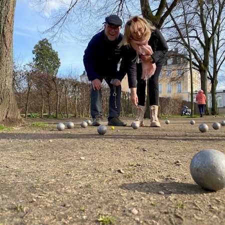 Zwei Menschen spielen Boule in einem Park.