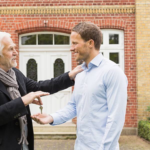 Vater überreicht seinem Sohn einen Schlüssel vor einem Haus