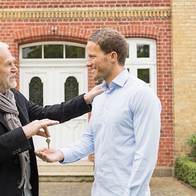 Vater überreicht seinem Sohn einen Schlüssel vor einem Haus