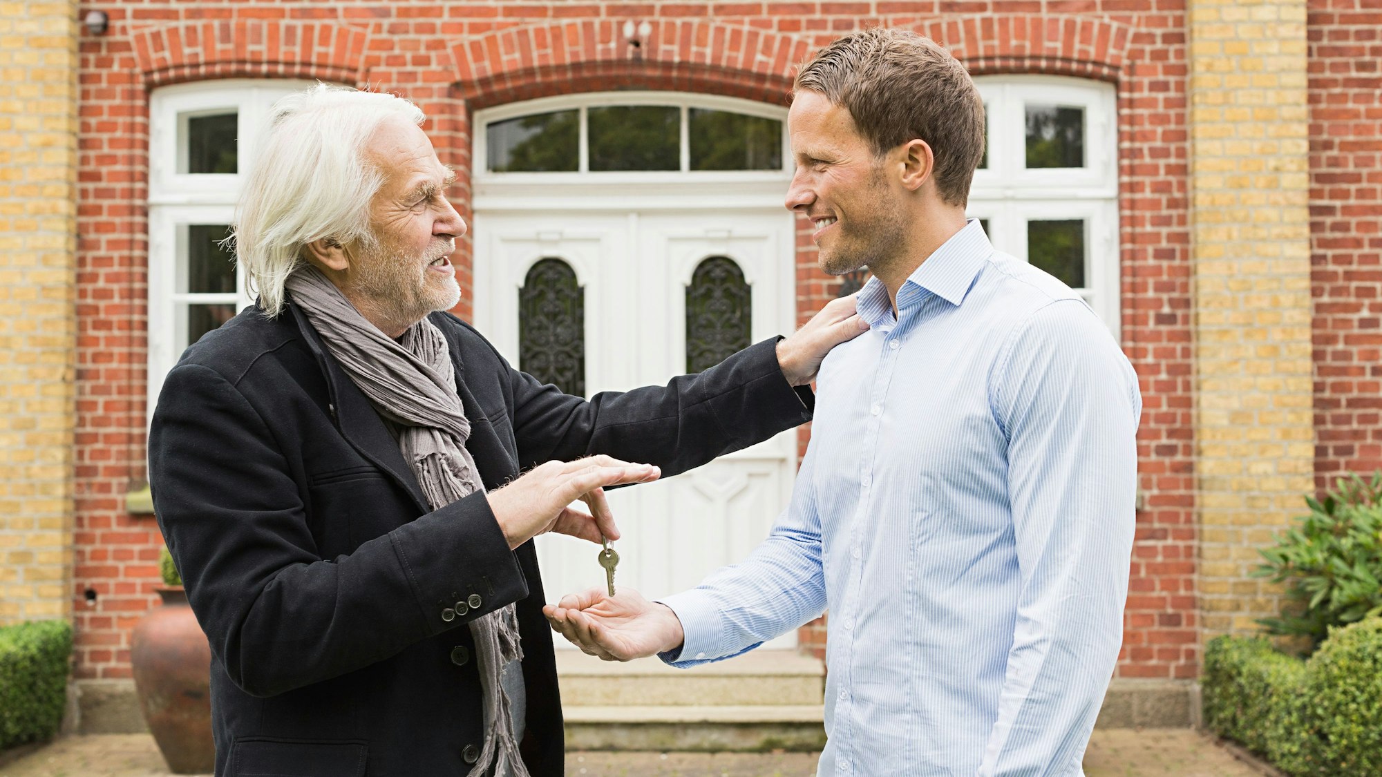 Vater überreicht seinem Sohn einen Schlüssel vor einem Haus