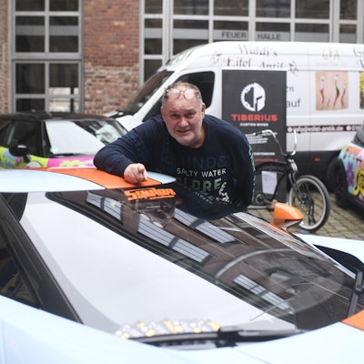 80-Euro-Waldi (Walter Lehnertz) steht an einem Sportwagen vor seiner neuen Galerie in Euskirchen.