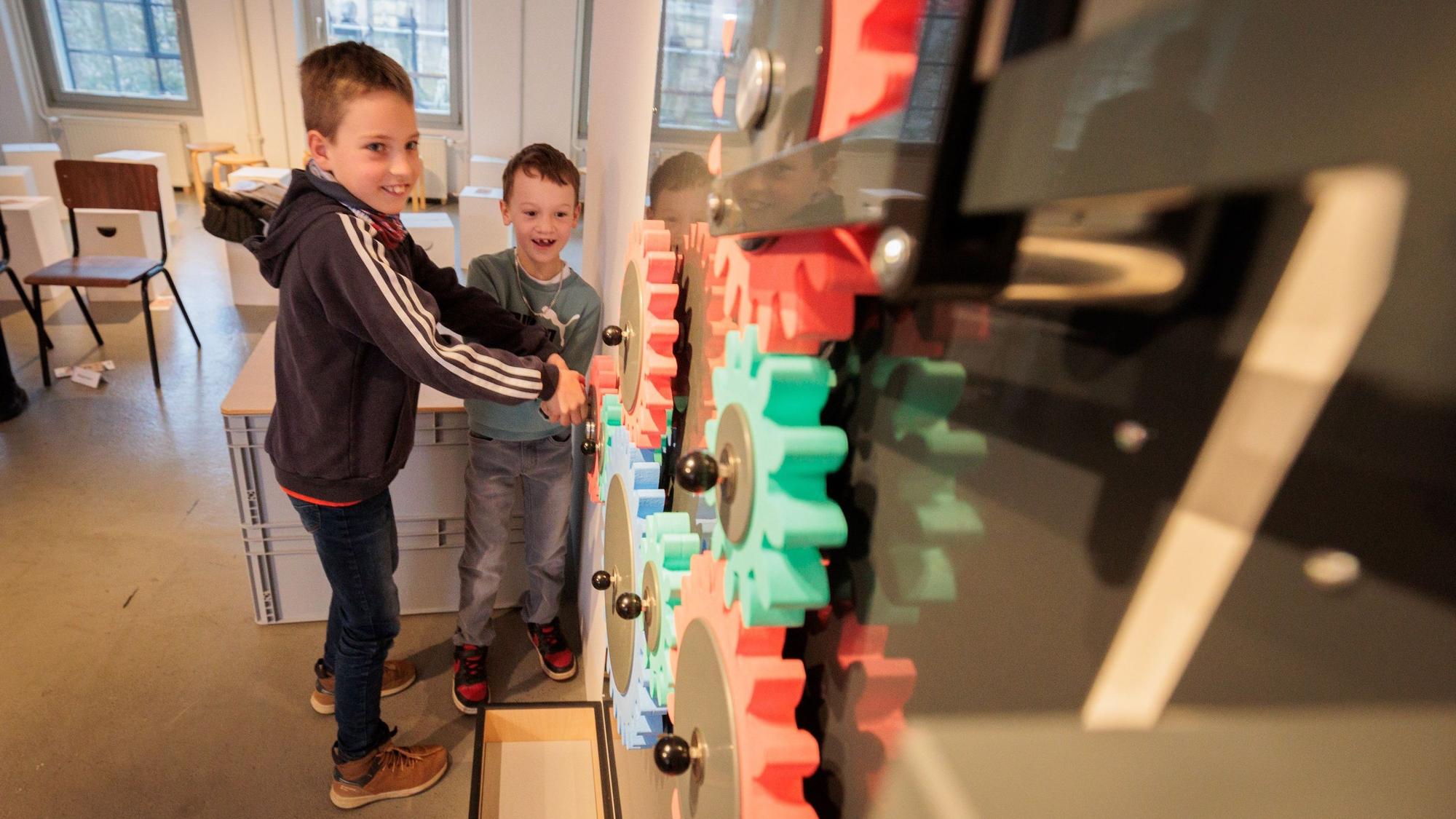 Zwei Jungen stehen an mehreren bunten Zahnrädern.