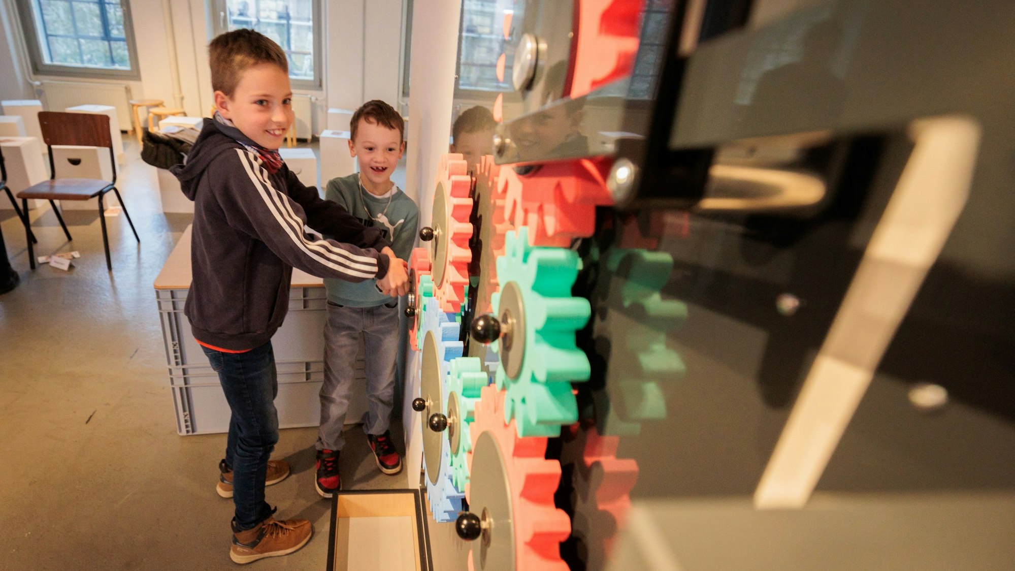 Zwei Jungen stehen an mehreren bunten Zahnrädern.